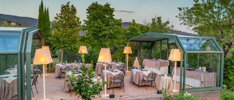 Een terras met tafels en stoelen, omgeven door glazen constructies en potplanten.