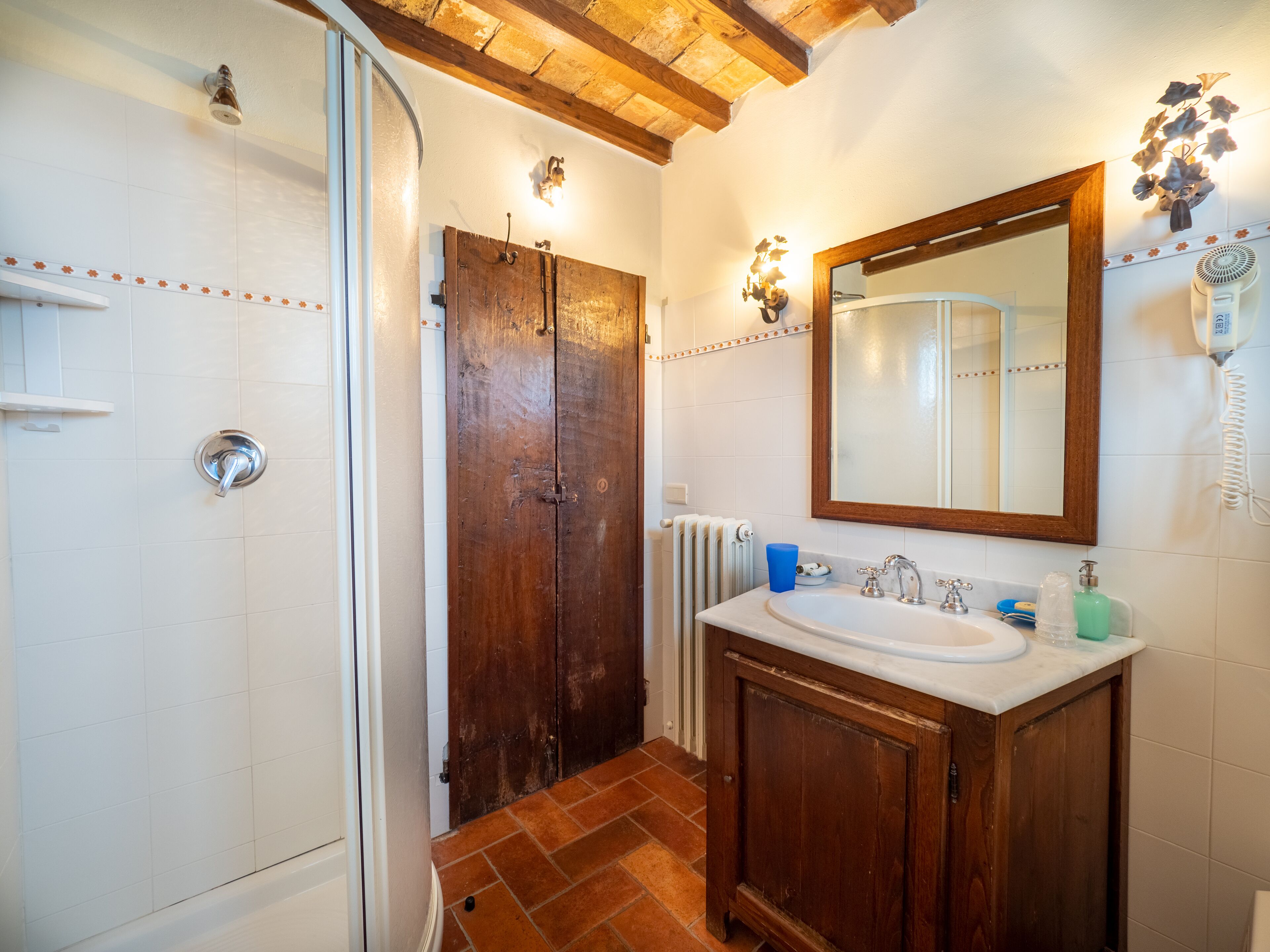 A bathroom with a wooden door, a white sink with a mirror, and a shower area.
