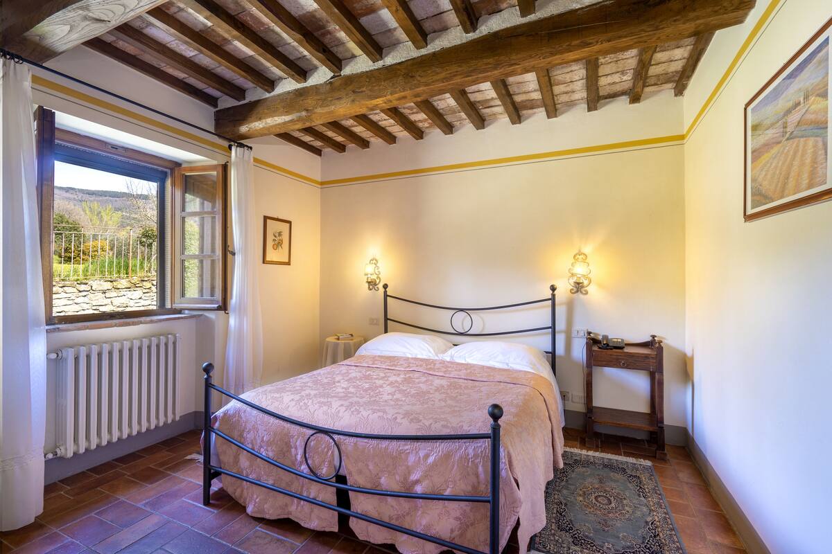 Une chambre à coucher avec un lit, une fenêtre avec des rideaux, un radiateur, une table de chevet et un luminaire fixé au mur.
