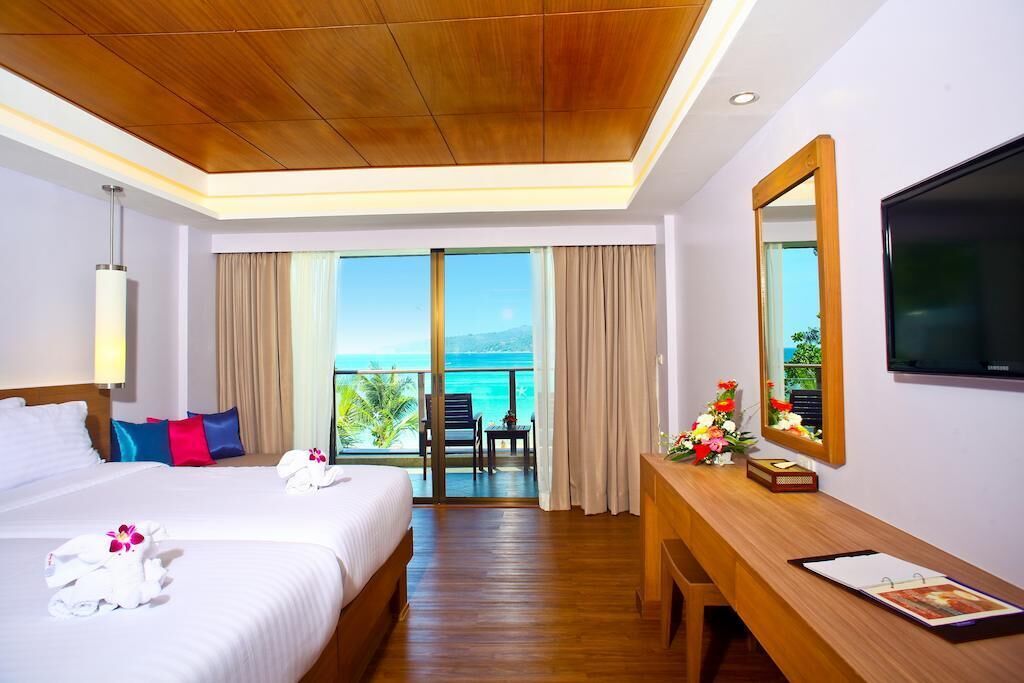 A hotel room with a bed, a desk, a TV, a balcony with a view of the sea, and a large mirror.