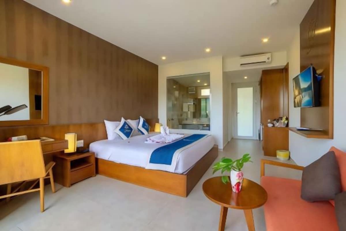 Een moderne hotelkamer met een groot bed, een bureau, een stoel, een kleine tafel met een plant en een televisie aan de muur.