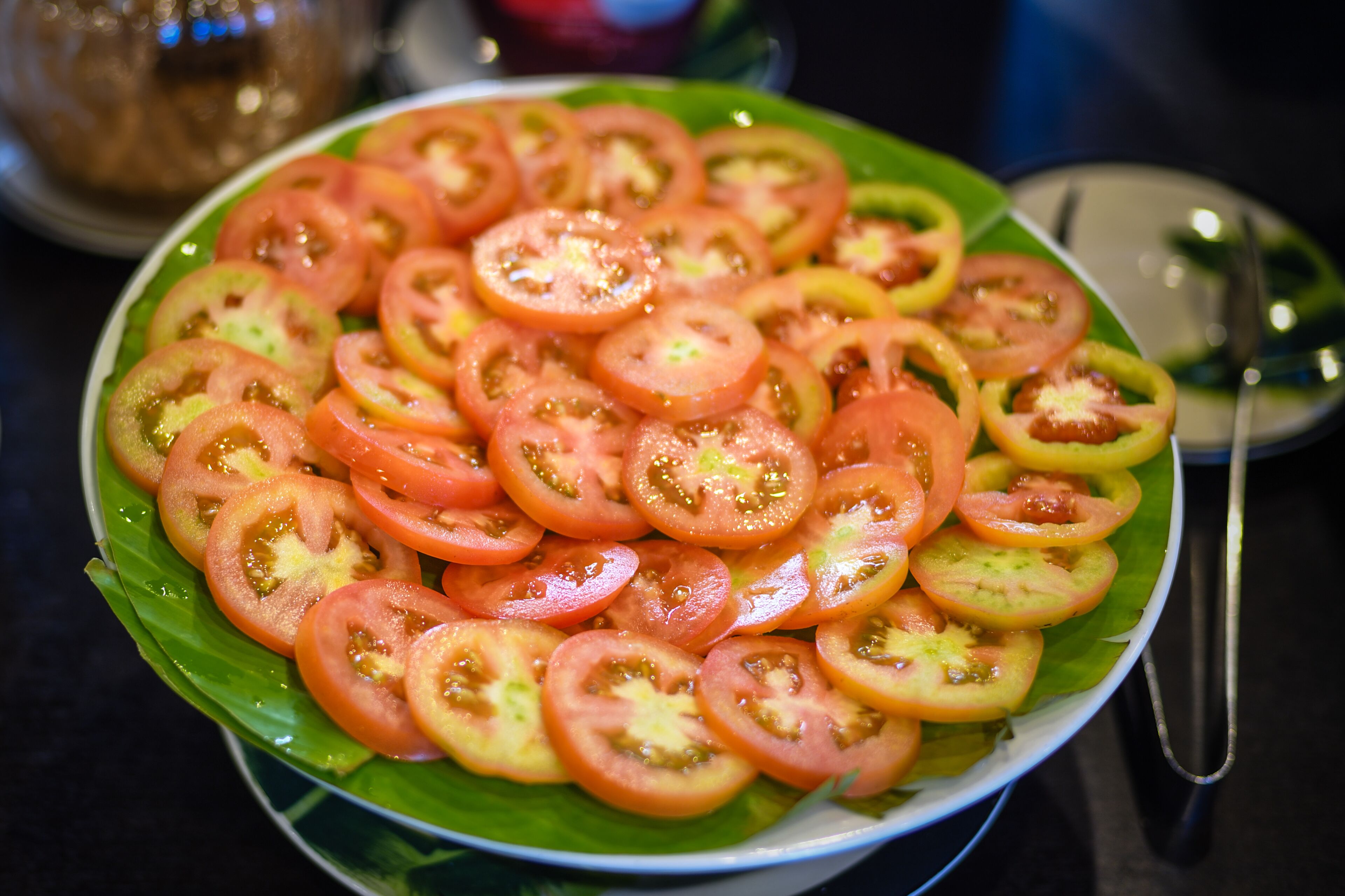 A plate of sliced tomatoes arranged on a green leaf.