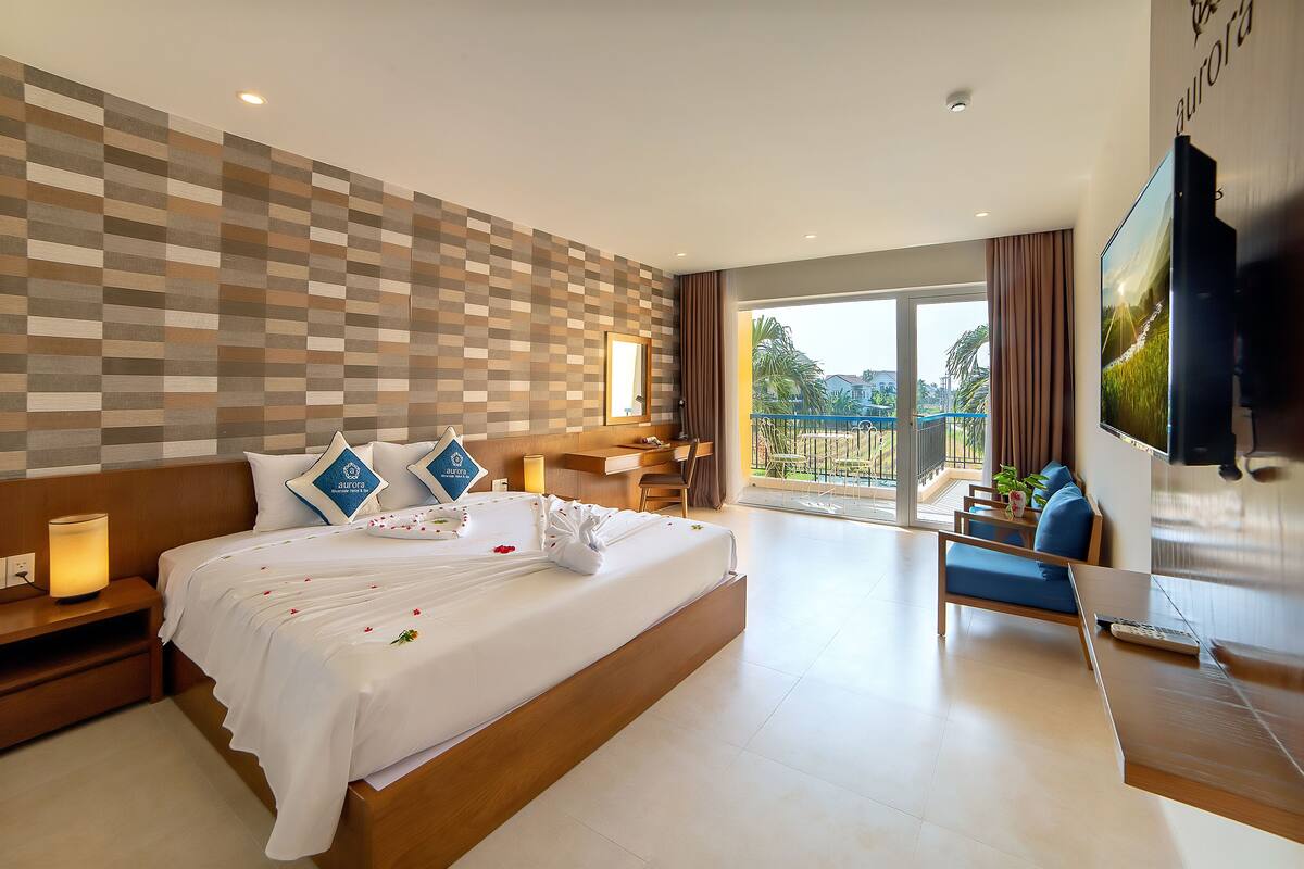 Quarto de hotel com cama grande, escrivaninha, cadeira, televisão e varanda com vista.