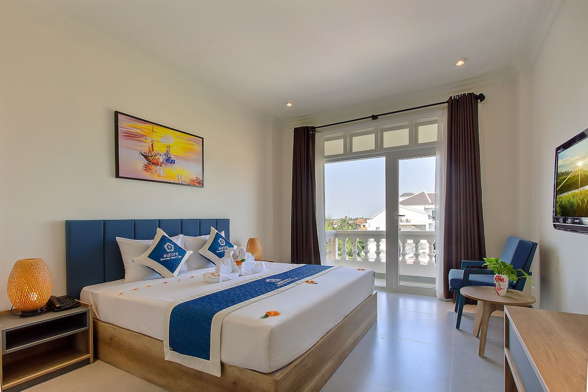 Quarto de hotel com cama, escrivaninha, cadeira, varanda e um quadro na parede.