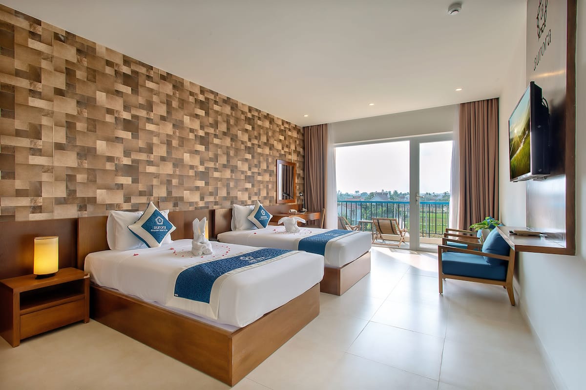 Quarto de hotel com duas camas, televisão, secretária e varanda com vista.