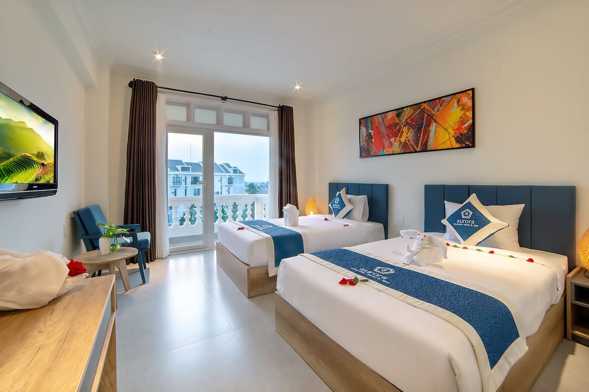Quarto de hotel com duas camas, uma escrivaninha, uma cadeira e varanda com vista para edifícios.