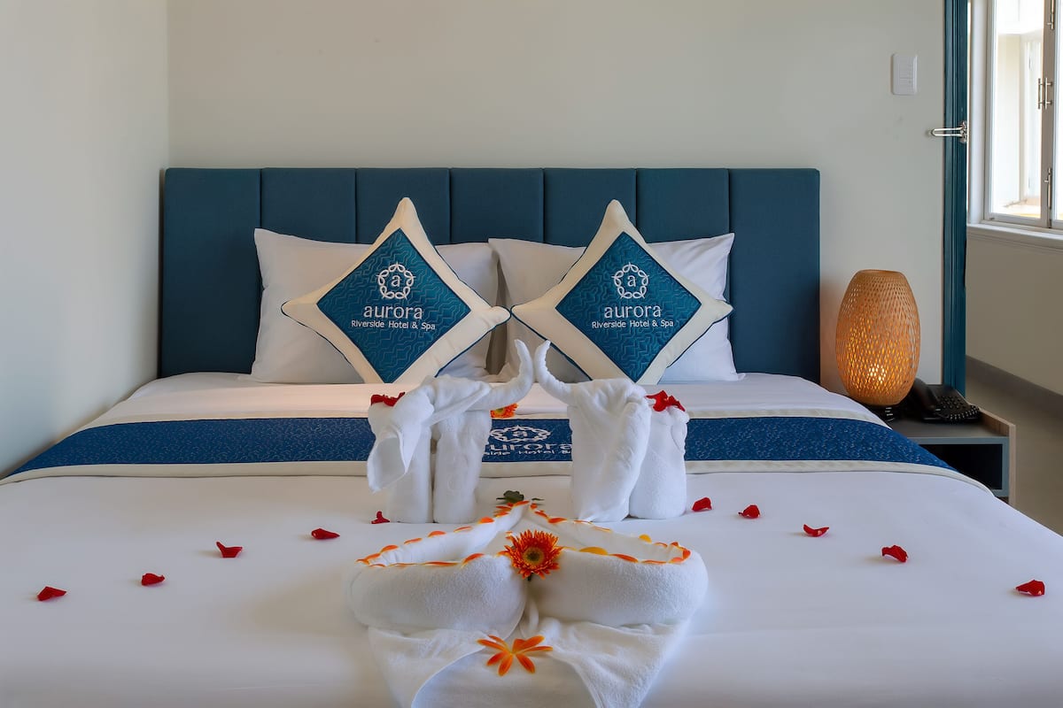 Quarto de hotel com cama, arranjo decorativo de toalhas e logotipo nos travesseiros.