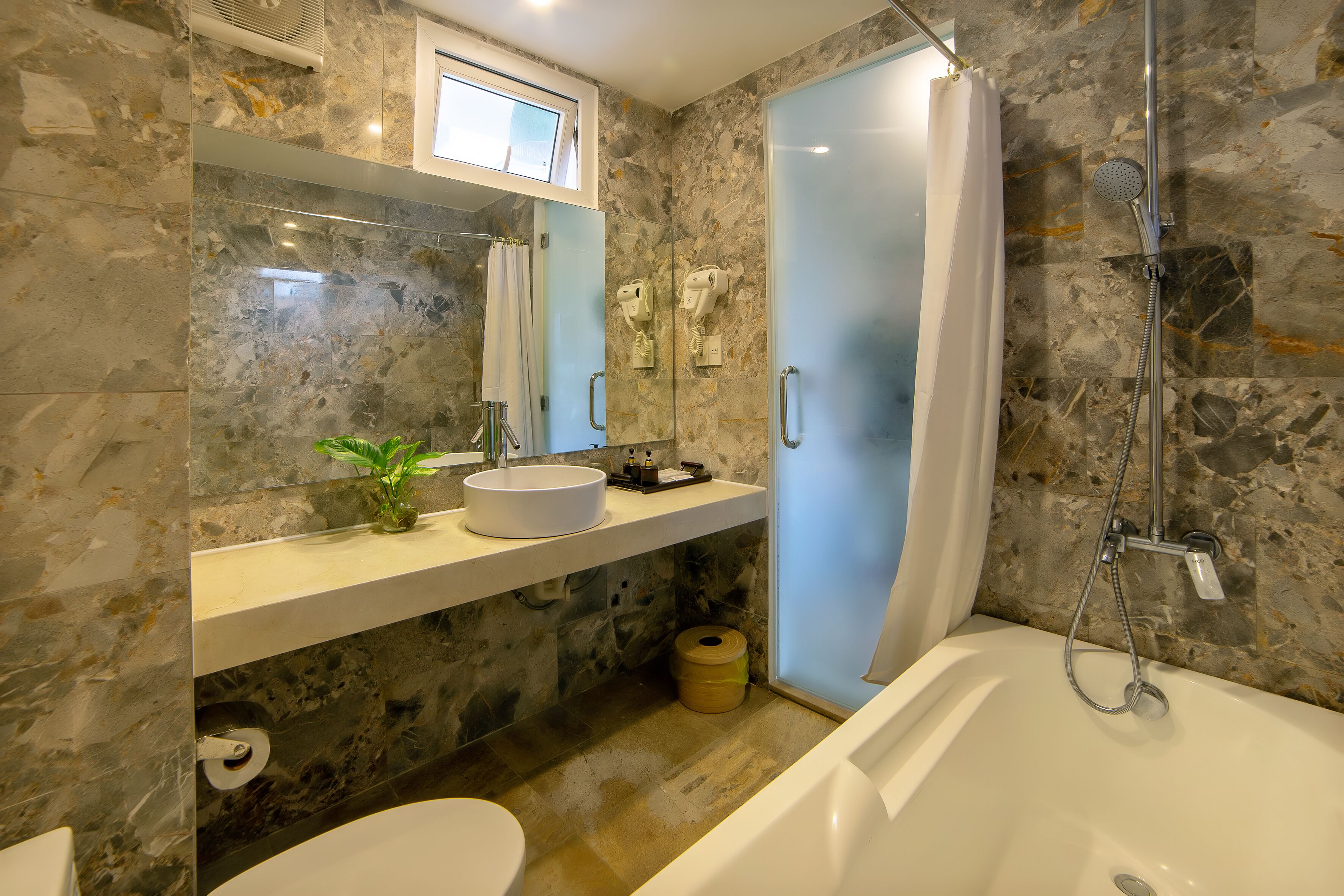 A bathroom with a marble wall, a white sink, a toilet, a shower, and a towel rack.