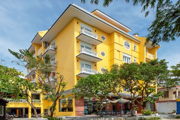 Um edifício amarelo de vários andares com varandas, mesas ao ar livre e uma fachada visível.