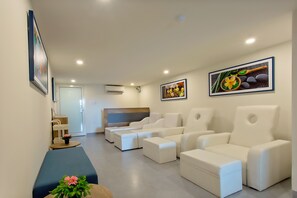 Uma área de relaxamento moderna com sofás e pufes de couro branco, um banco de madeira com planta em vaso e obras de arte emolduradas nas paredes.