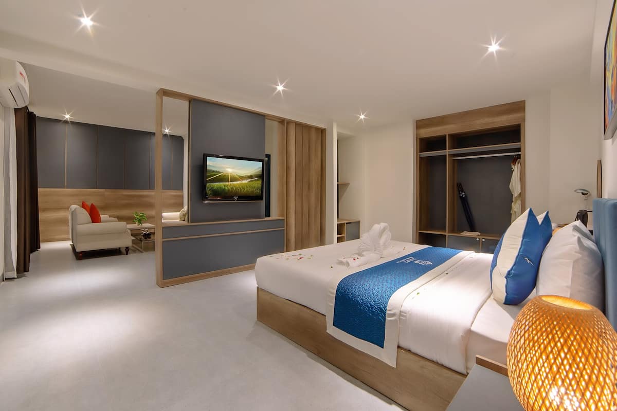 Quarto de hotel moderno com uma cama grande, televisão, guarda-roupa e área de estar.