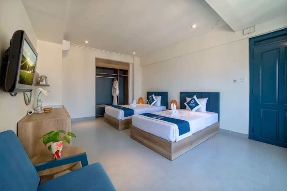 Een hotelkamer met twee bedden, een televisie, een kledingkast en een zithoek met een plant.