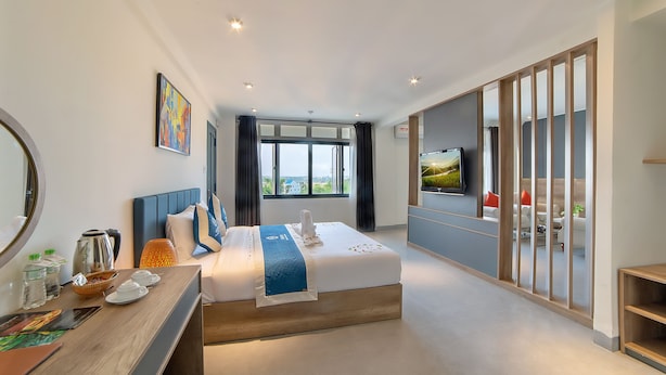 A modern hotel room with a large bed, a desk with a coffee maker, a TV, and a view of the outdoors. - Aurora Riverside Hotel and Spa (Da Nang)