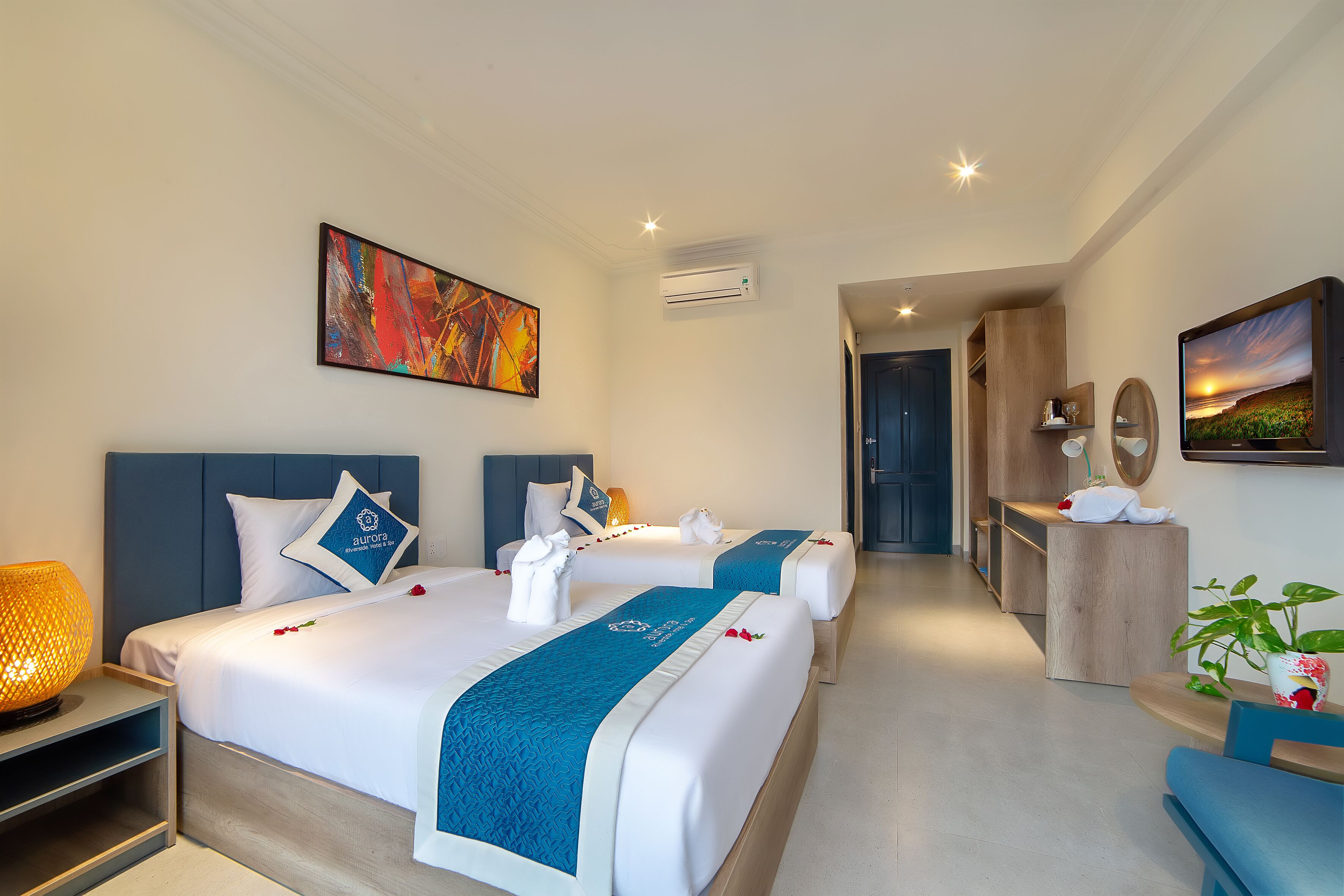 Een hotelkamer met twee bedden, een bureau, een stoel, een lamp en kunstwerken aan de muur.