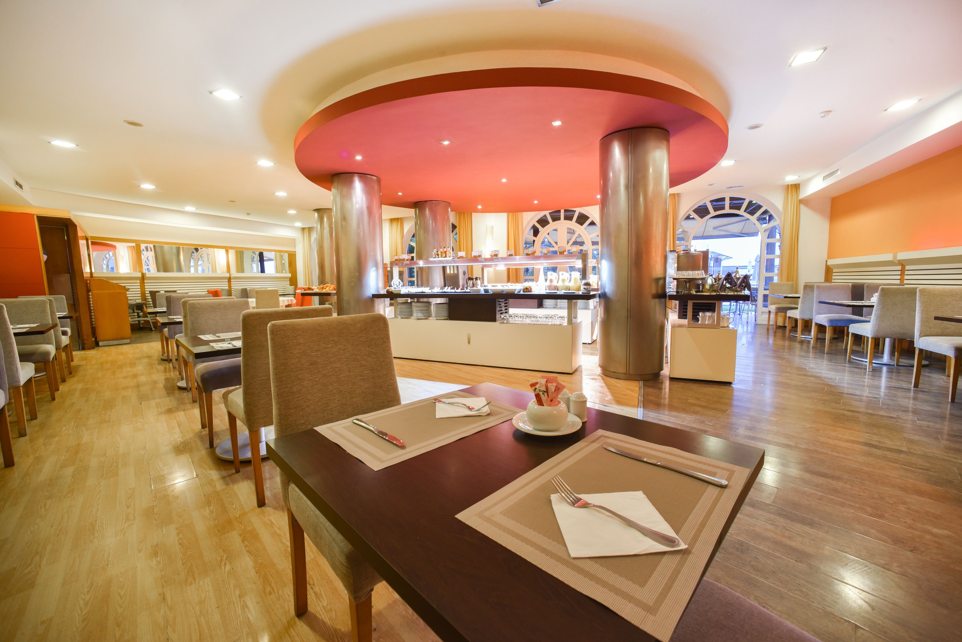 A spacious restaurant with wooden flooring, multiple dining tables, and a central kitchen area.