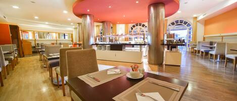 Un restaurante espacioso con suelo de madera, varias mesas de comedor y una zona de cocina central.