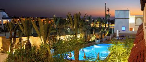 A pool area with palm trees and a sunset view.