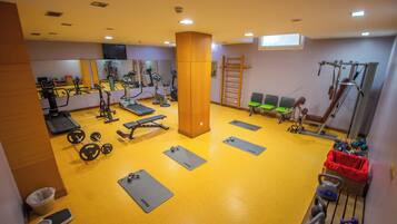 Un gimnasio con diversos equipos de ejercicio, incluyendo cintas de correr, bicicletas estáticas y pesas libres.