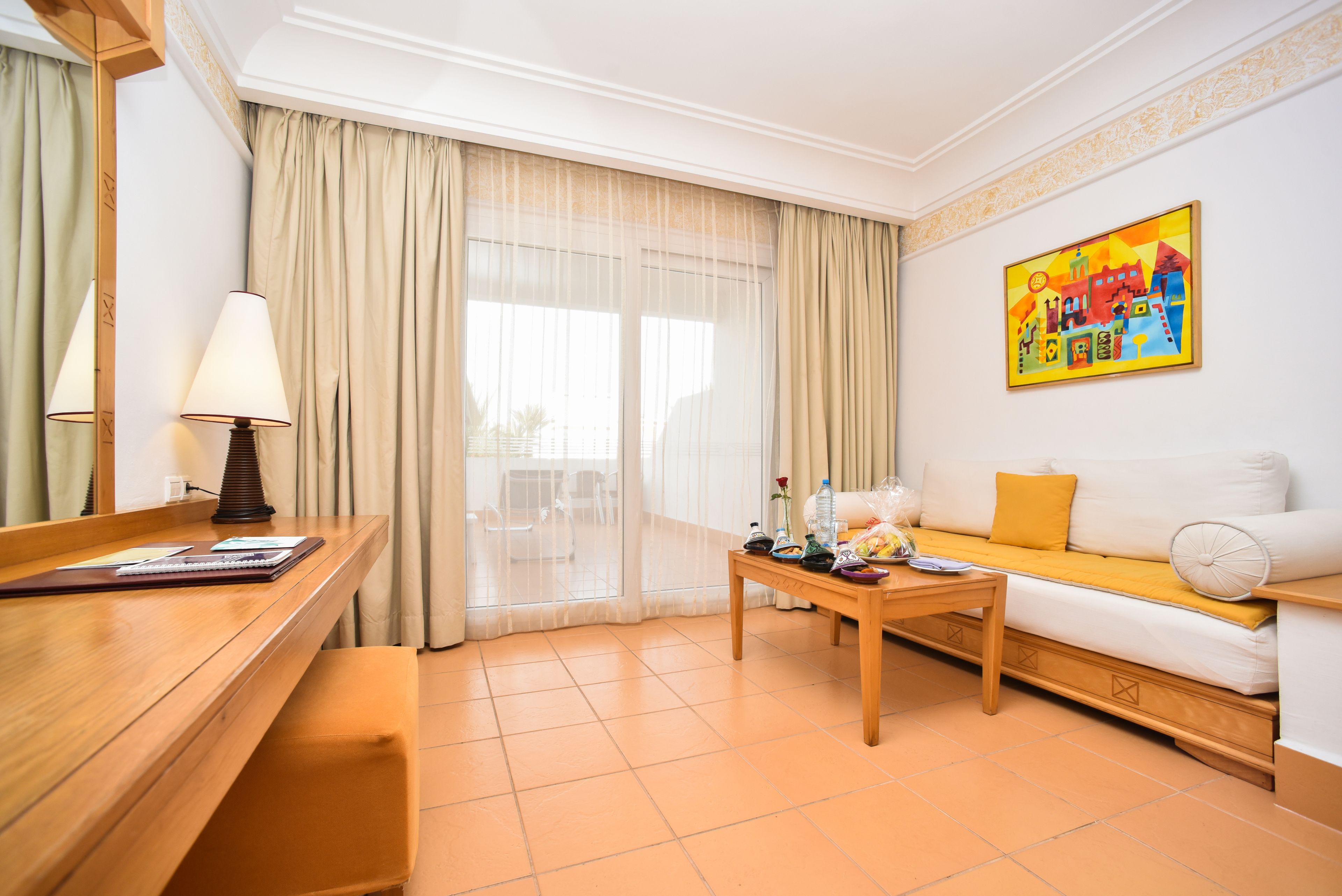 A hotel room with a wooden desk, a sofa, a coffee table, and a painting on the wall.