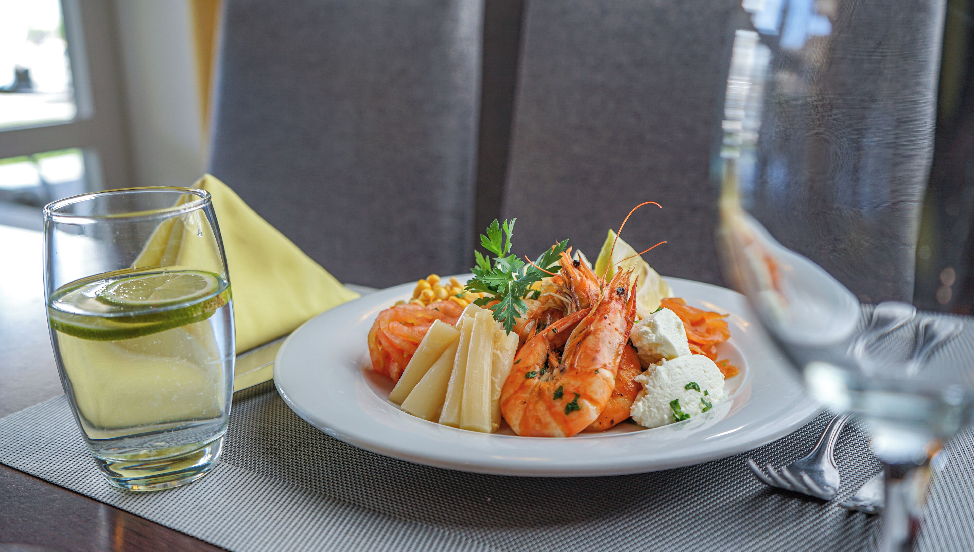 A plate of shrimp with lemon slices and parsley, a glass of water, and a napkin on a table.