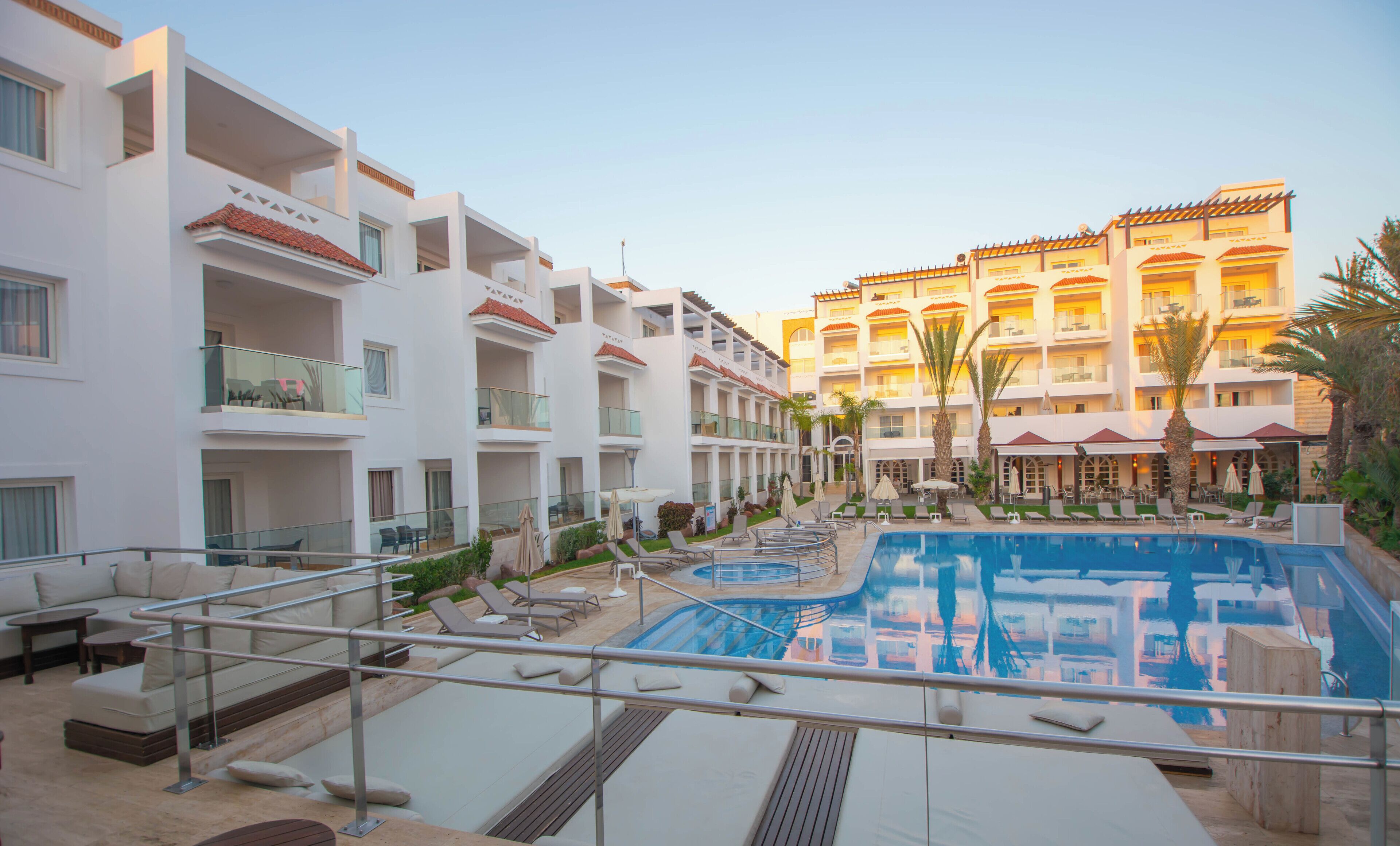 A hotel with multiple balconies, a swimming pool, and outdoor seating areas.