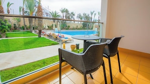 A balcony with a glass railing, a round table, two chairs, and a view of a swimming pool and greenery. - Timoulay Hotel & Spa Agadir (Agadir)