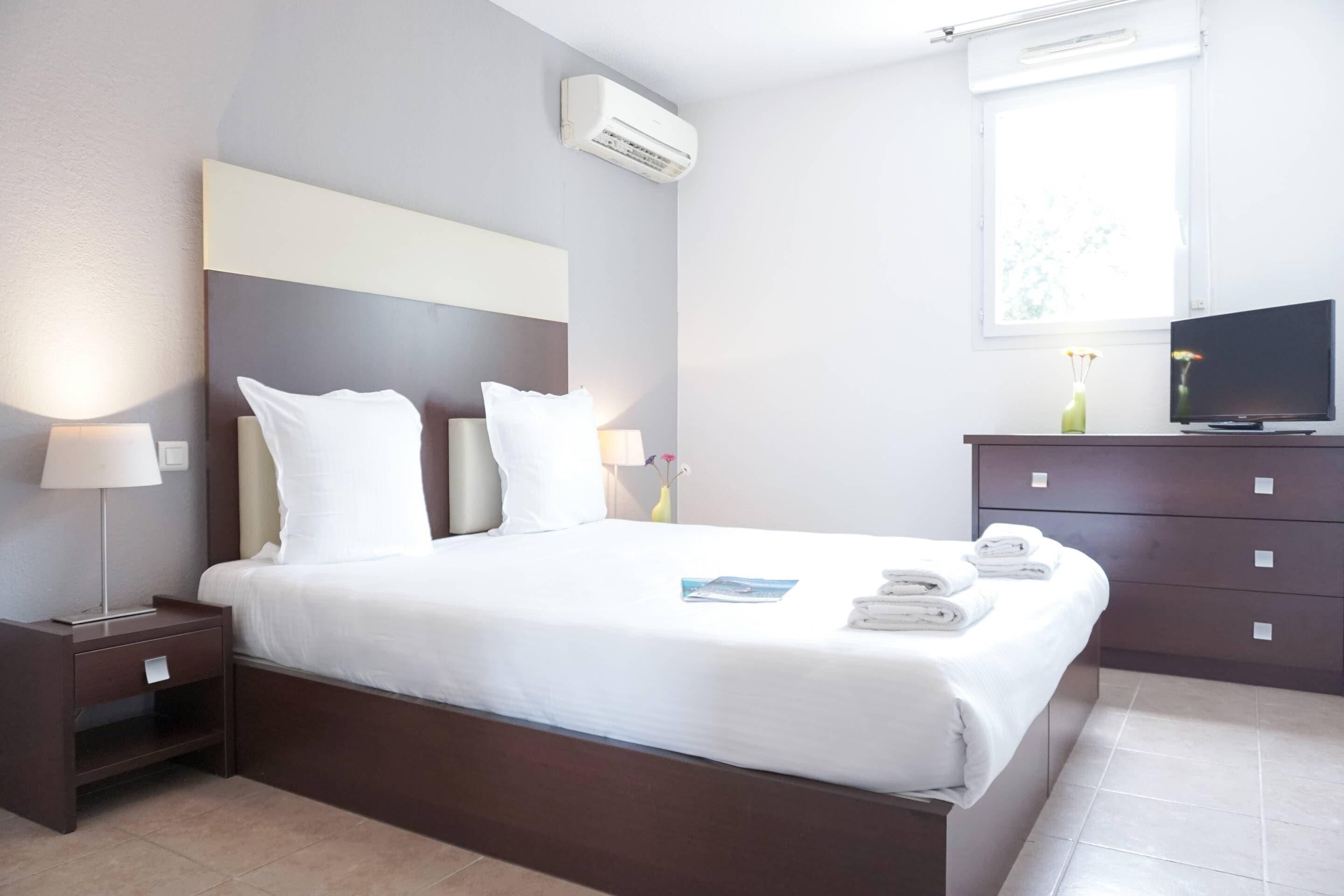 A hotel room with a bed, bedside tables, a TV, and a window.