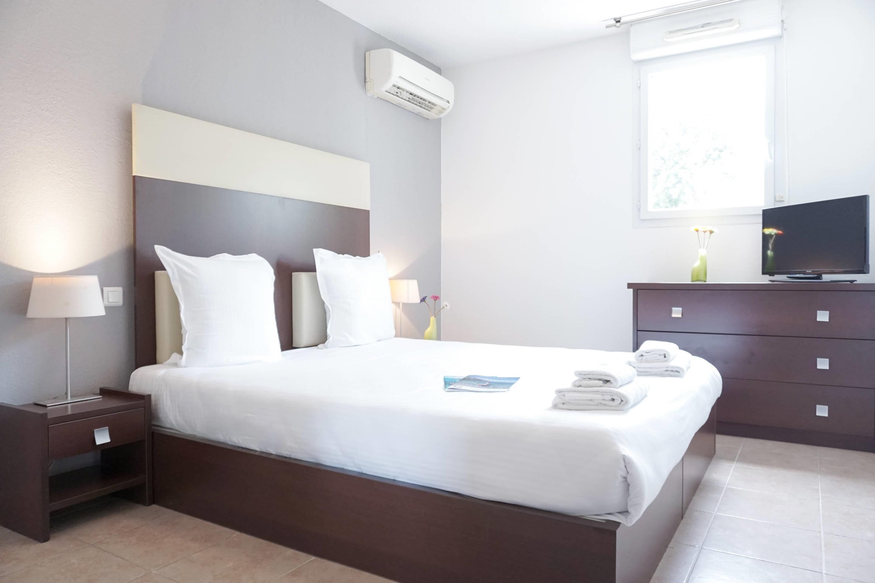 Une chambre d’hôtel équipée d’un lit, d’une table de chevet, d’une commode, d’une télévision et d’une fenêtre donnant sur un paysage agréable.