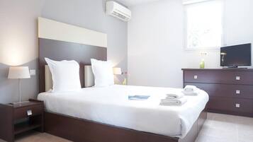 Une chambre d’hôtel équipée d’un lit, d’une table de chevet, d’une commode, d’une télévision et d’une fenêtre donnant sur un paysage agréable.