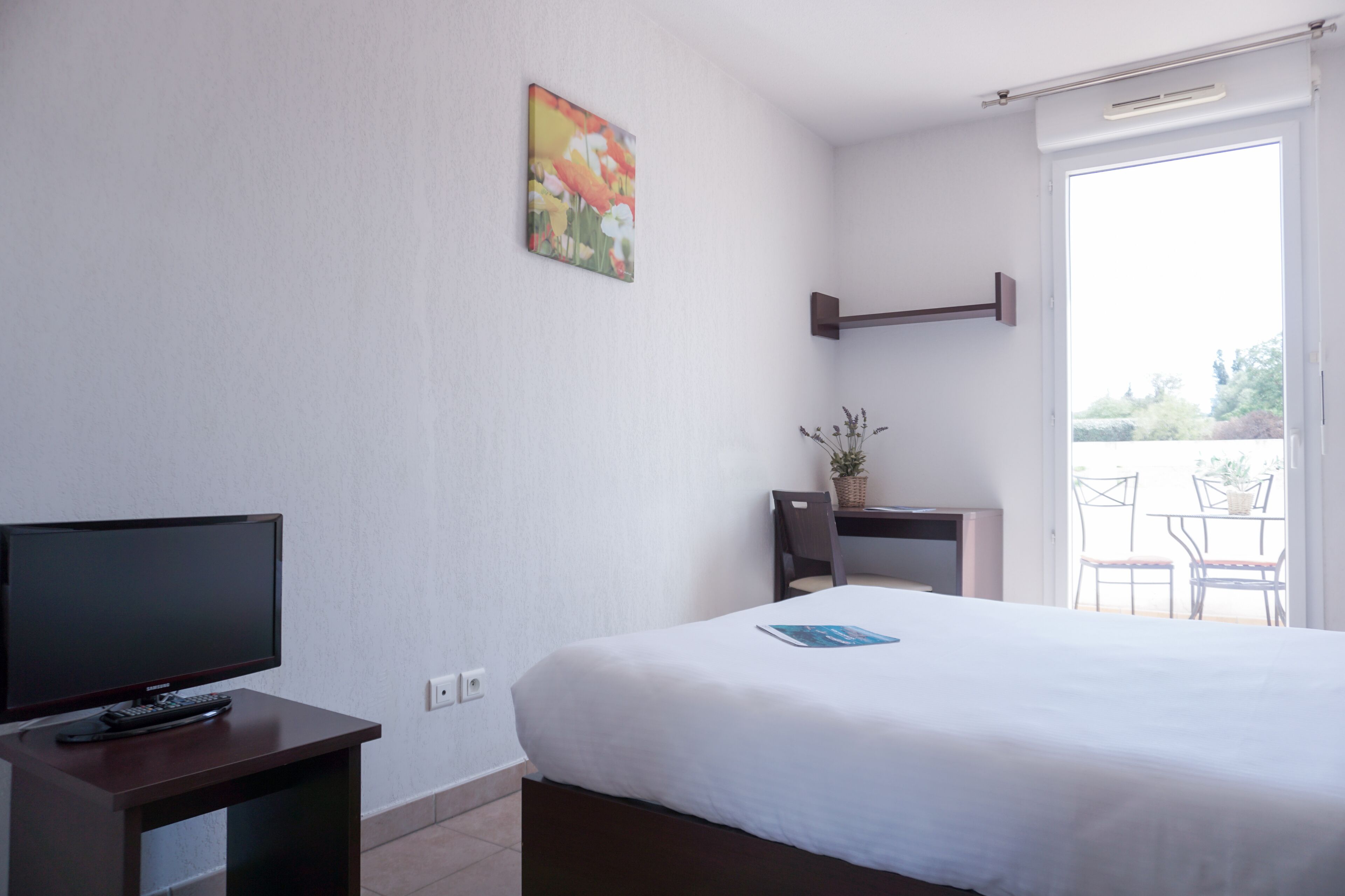 A hotel room with a bed, a TV, a desk, and a window with a view of the outdoors.