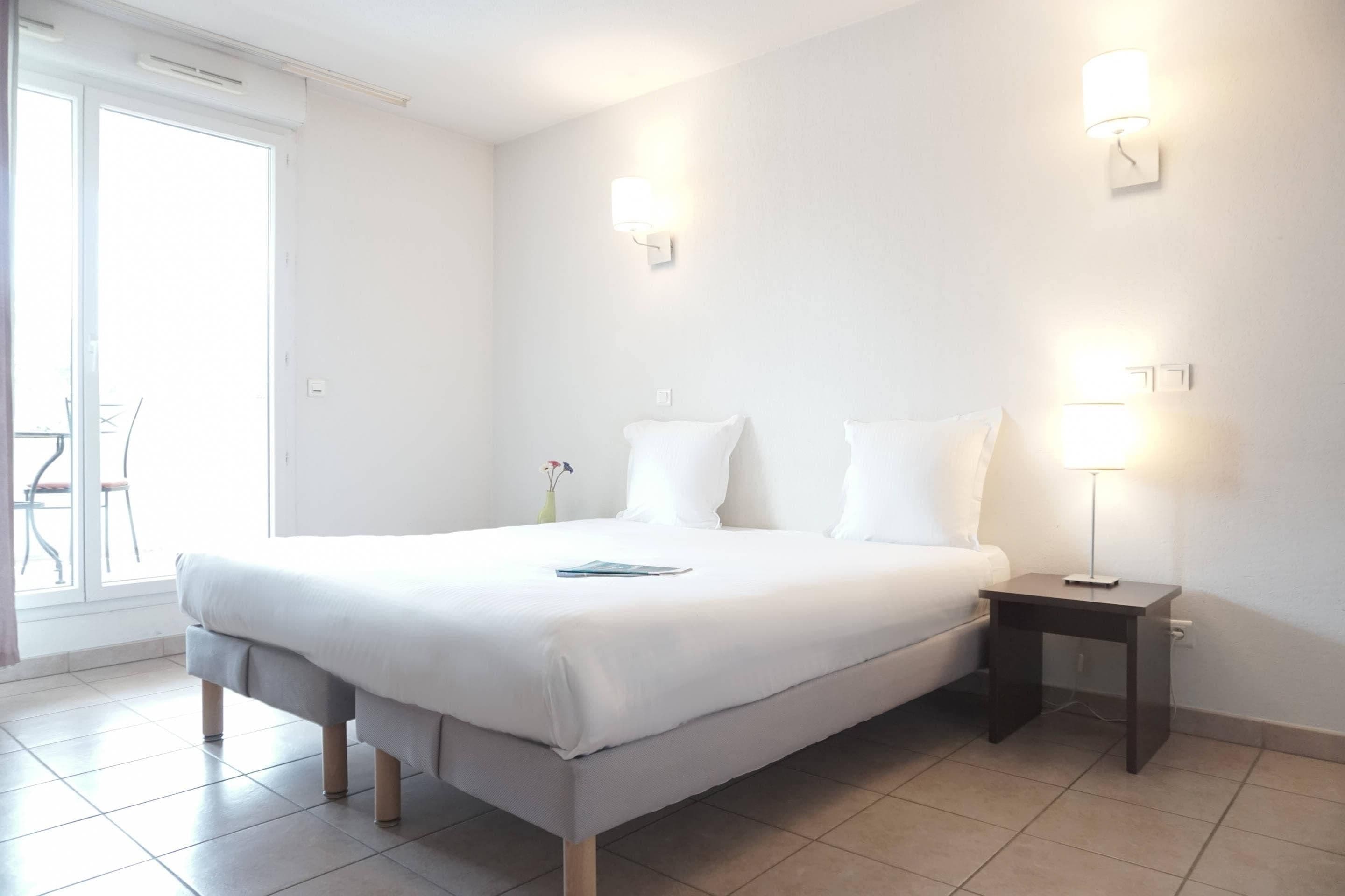 A hotel room with a bed, bedside tables, and a view of the outside.