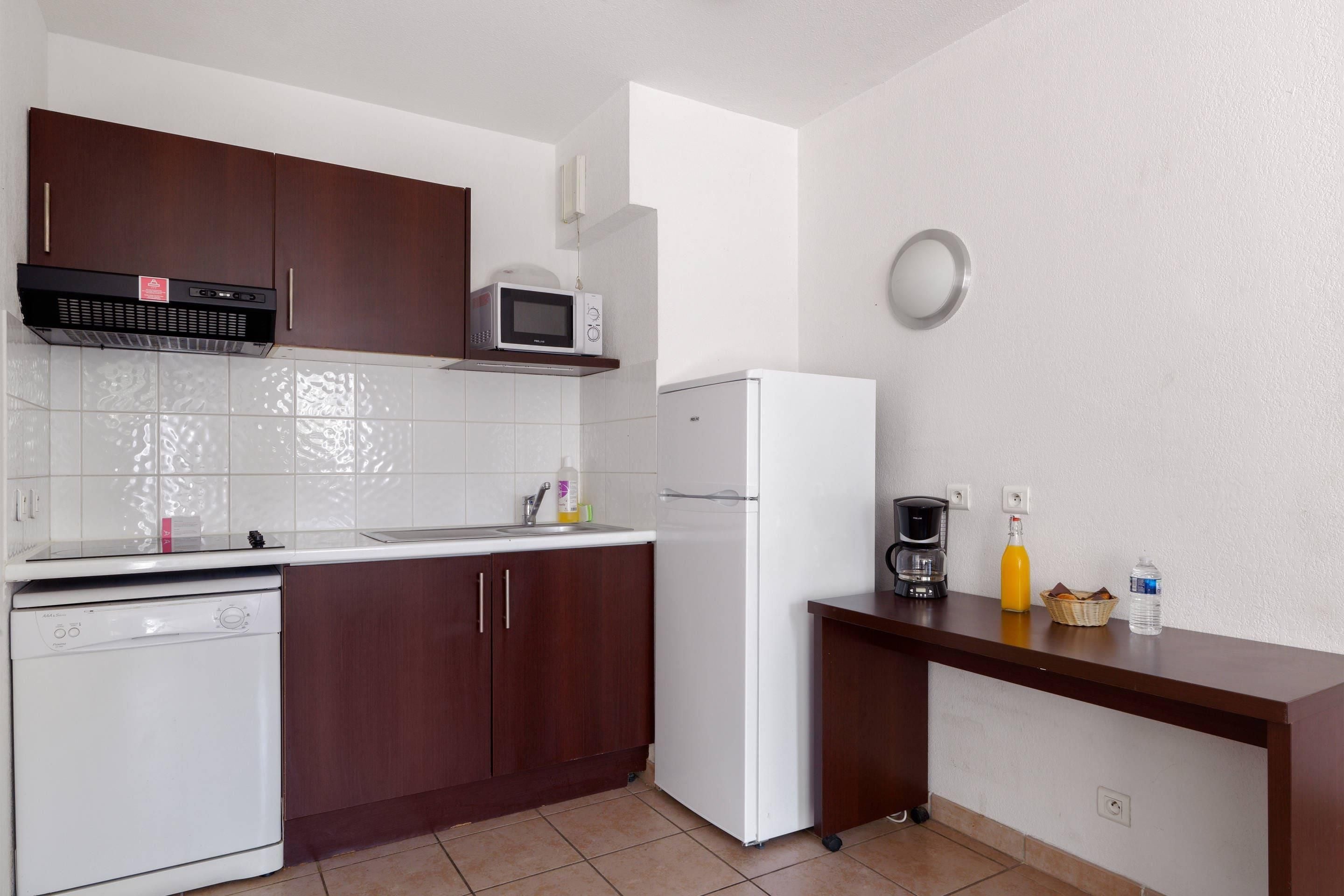 A compact kitchen with a dishwasher, microwave, refrigerator, and a coffee maker on the counter.