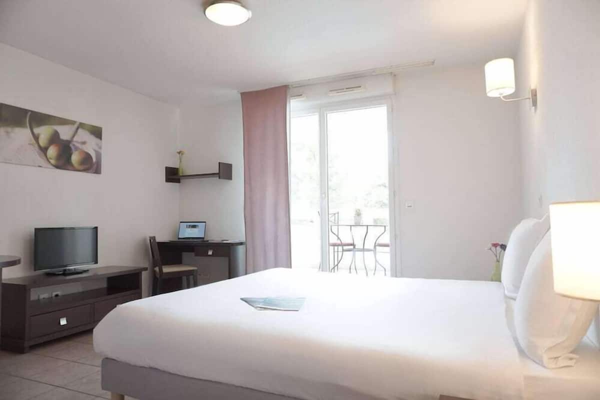 A hotel room with a bed, a desk with a computer, a television, and a window with a view of the outdoors.
