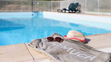 A poolside area with a towel, sunglasses, and a hat on the edge.