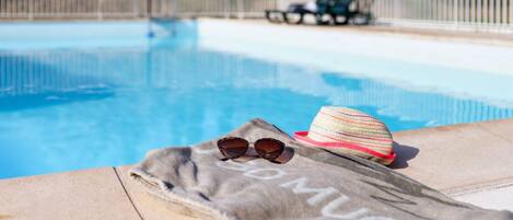 Zona de piscina con una toalla, gafas de sol y un sombrero al borde.
