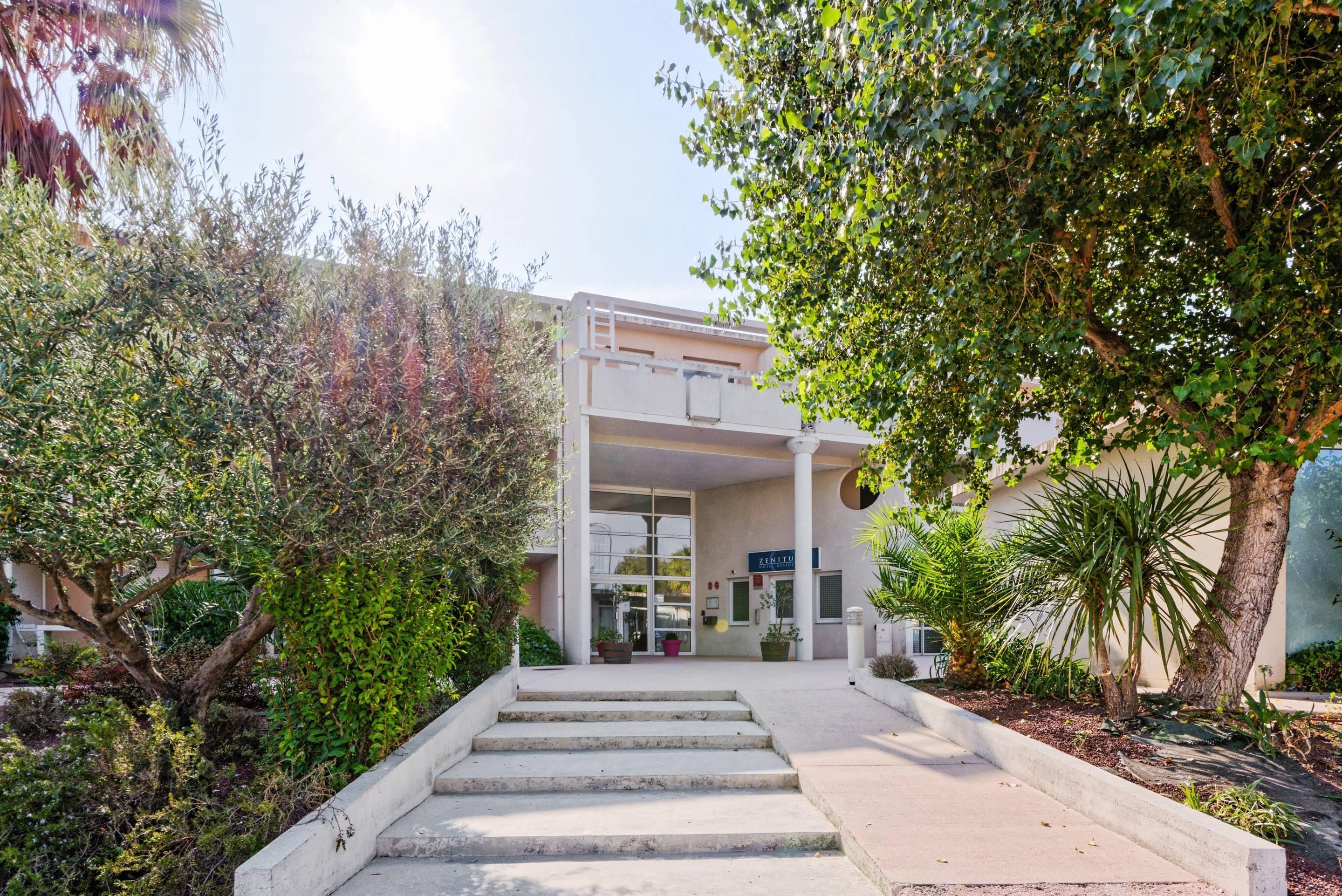 A building with a staircase leading to a door, surrounded by greenery.