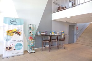 A modern hotel lobby with a reception desk, a glass display case, and a staircase. - Comfort Aparthotel Six-Fours (Six-Fours-les-Plages)