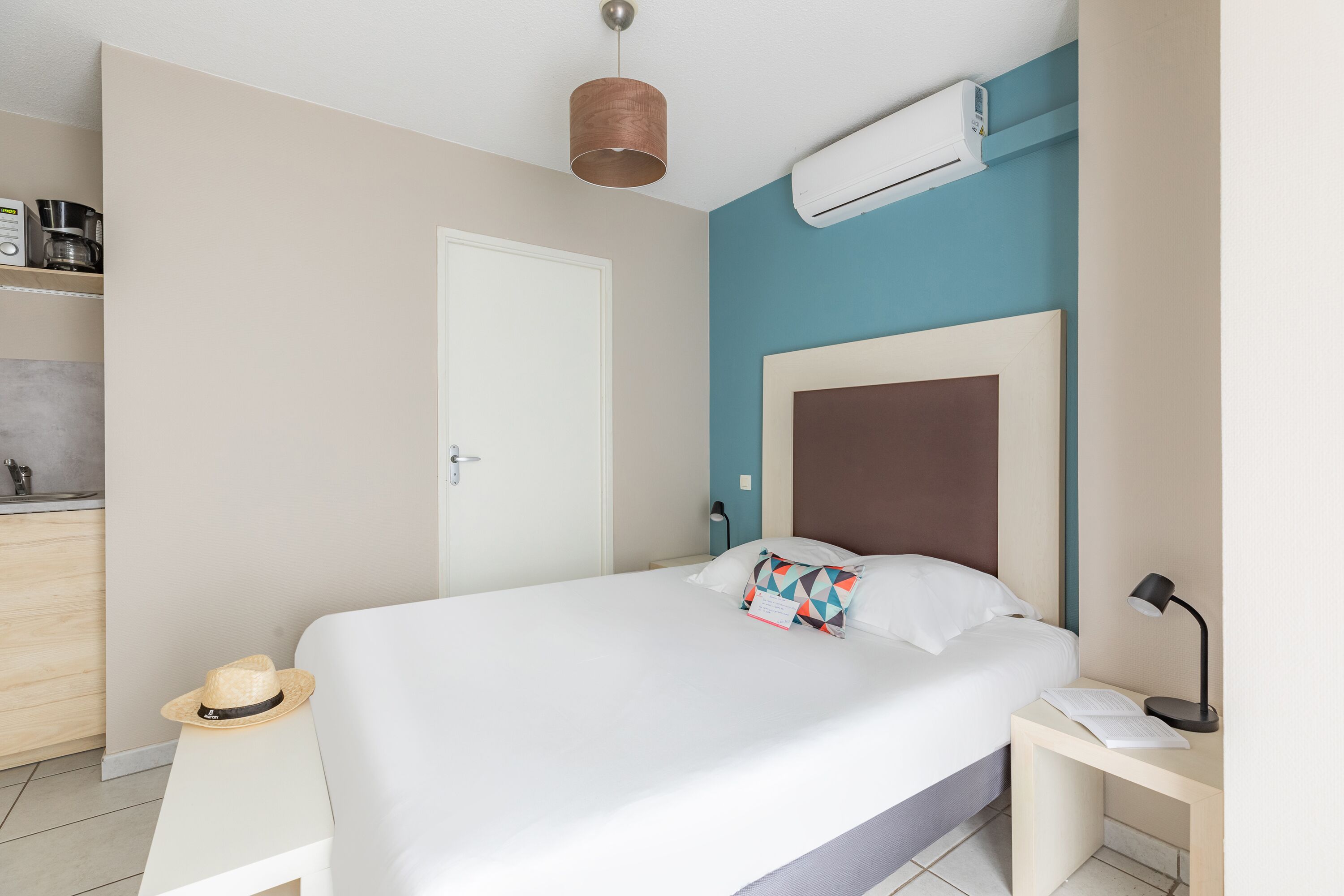 A bedroom with a bed, bedside table, lamp, and a hat on the floor.
