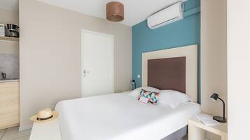 A bedroom with a bed, bedside table, lamp, and a hat on the floor.