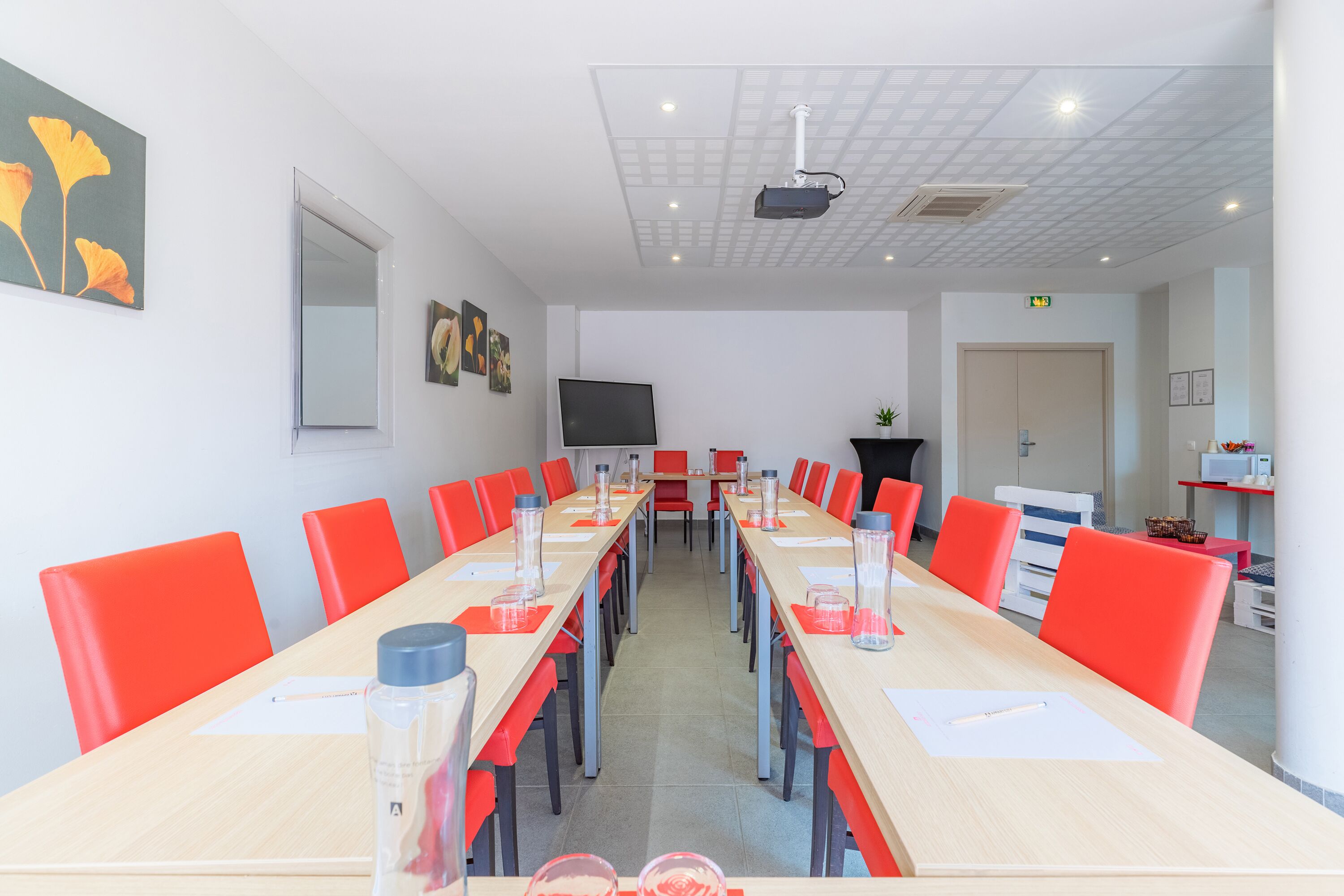 A conference room with a long table, red chairs, and a projector screen.