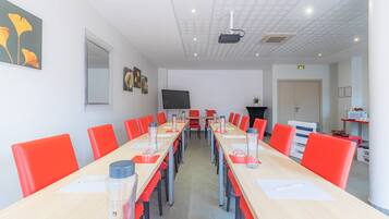 A conference room with a long table, red chairs, and a projector screen.