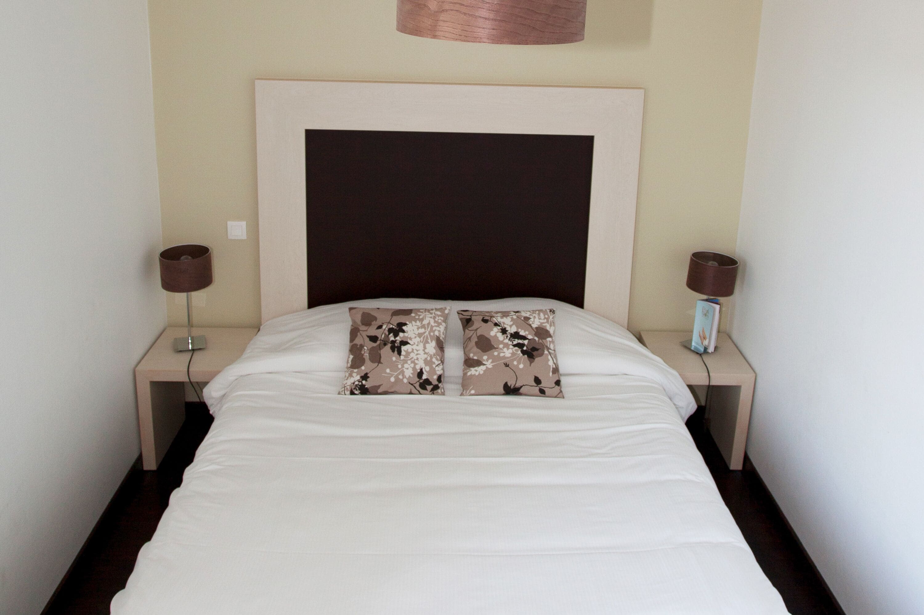 A neatly made bed with two floral pillows, a large headboard, and two bedside lamps on wooden nightstands.