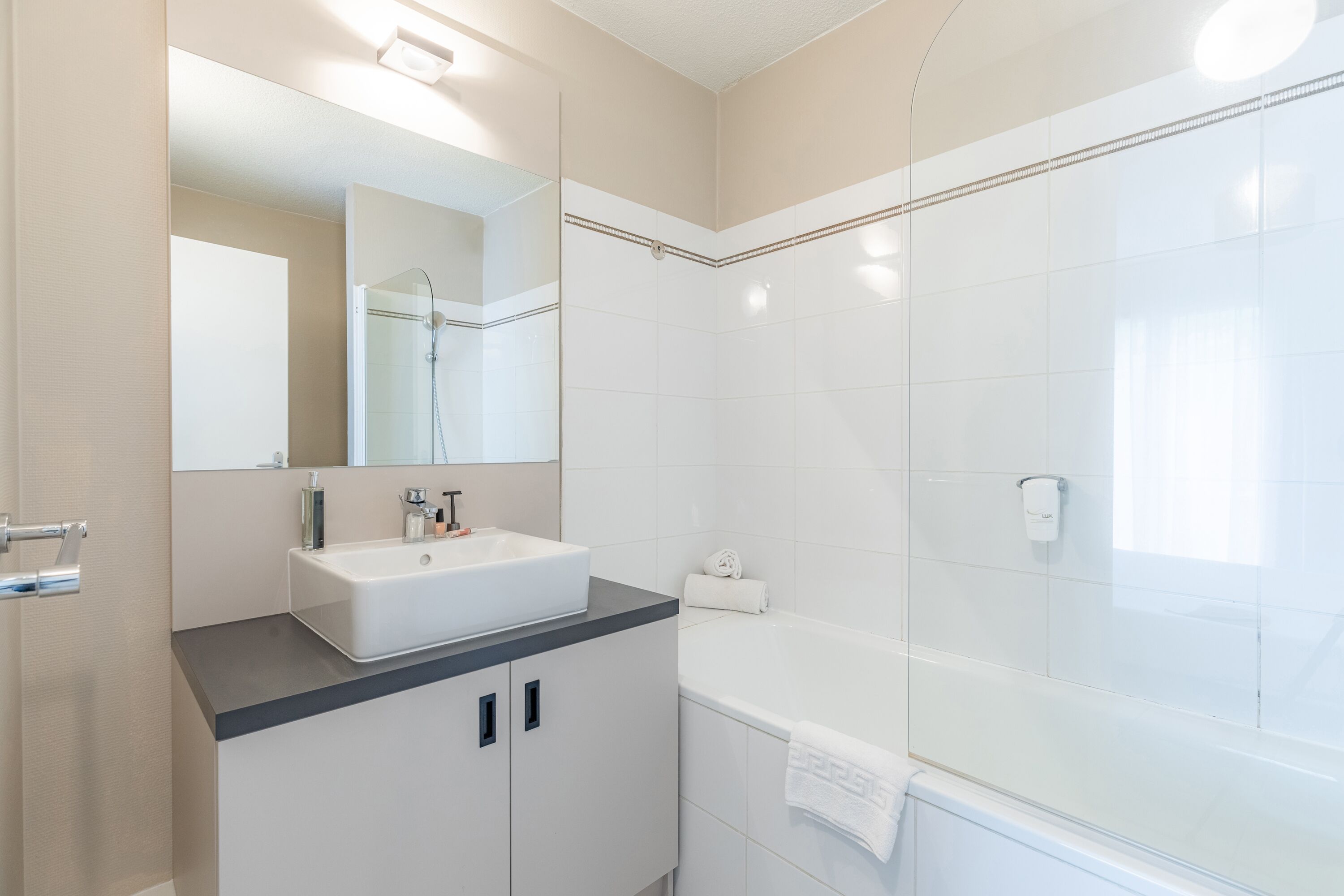 Un baño moderno con lavamanos, espejo y bañera blancos.
