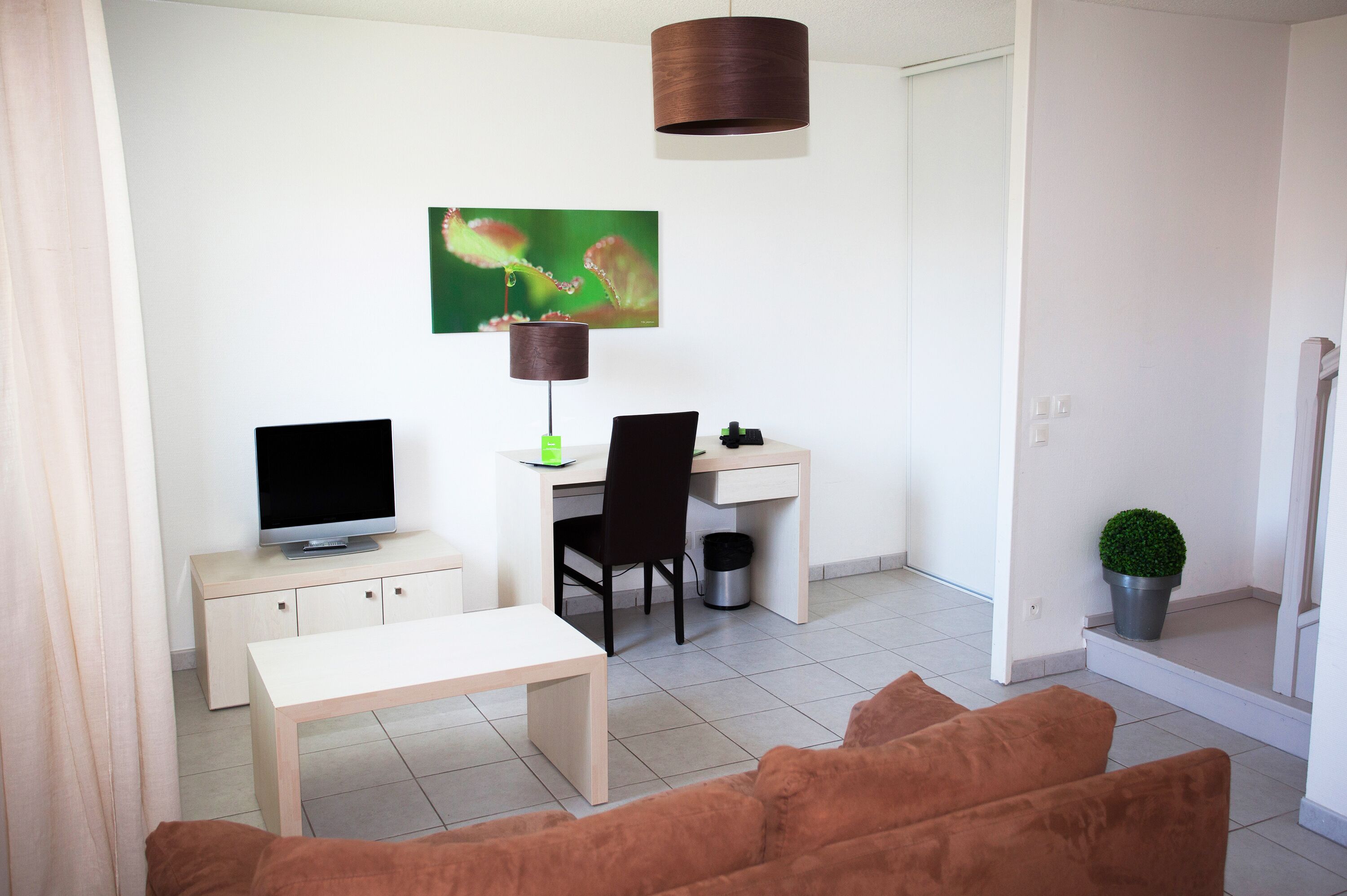 A modern living room with a TV, desk, and chair, a small table, and a sofa.