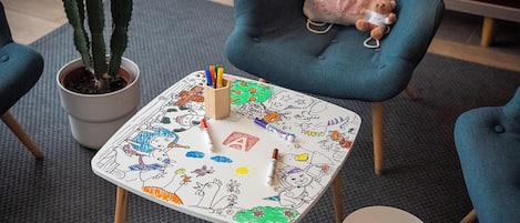 A small table with a colorful drawing pad, a cactus plant, a teddy bear, and a blue chair.