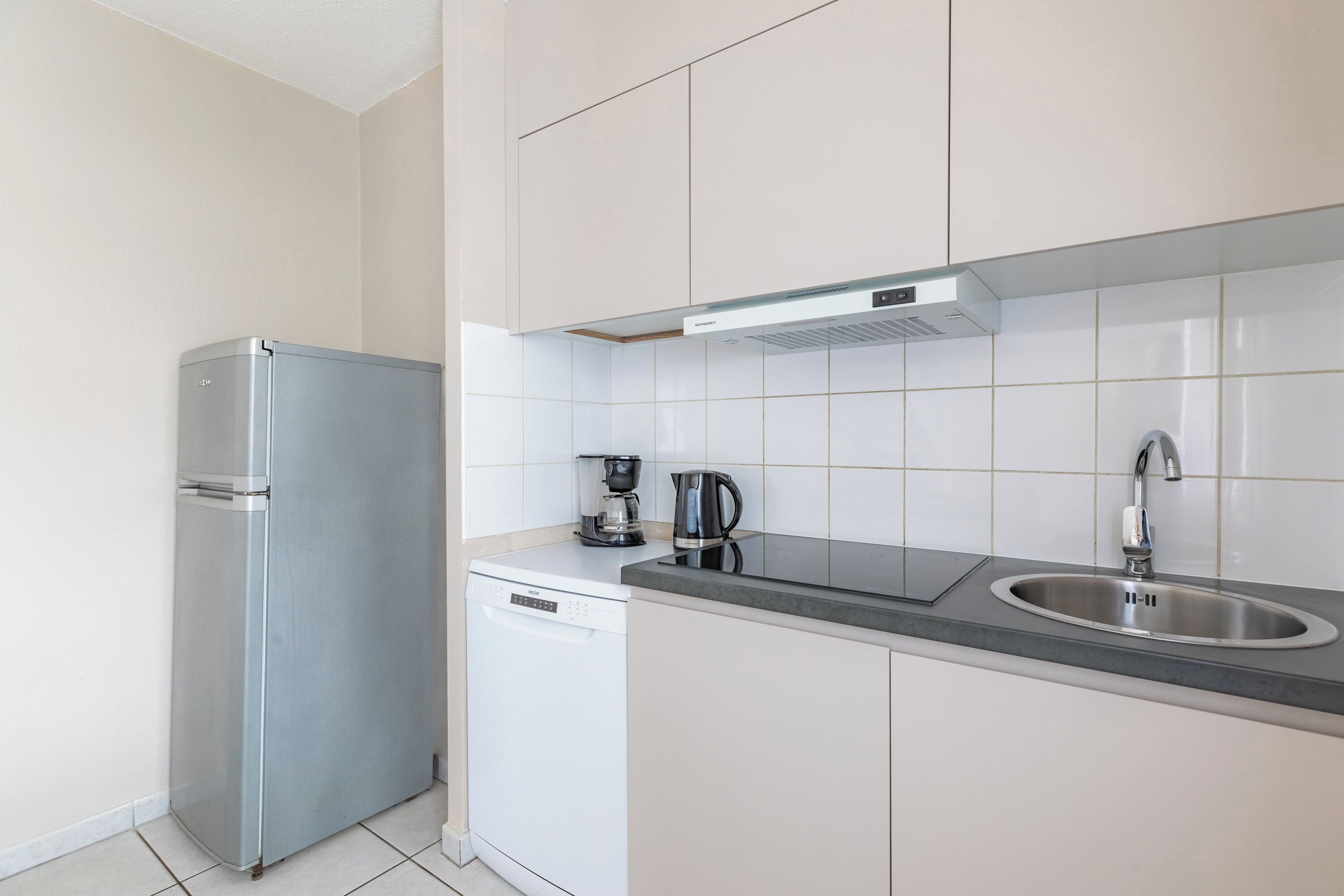 Una cocina compacta equipada con refrigerador, lavavajillas, cafetera y pileta.