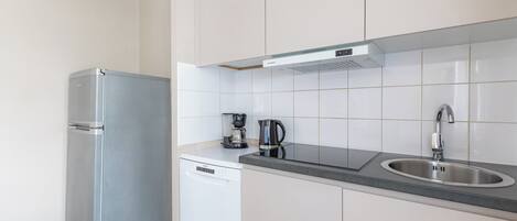 Una cocina compacta equipada con refrigerador, lavavajillas, cafetera y pileta.
