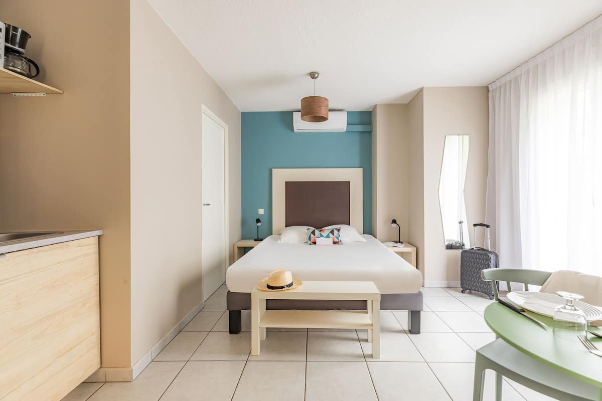 Ein Hotelzimmer mit Bett, Nachttisch und einem kleinen Esstisch mit Stühlen. Auf dem Boden liegen ein Koffer und eine Lampe.