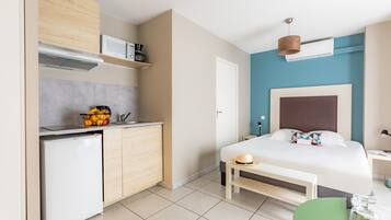 Een kleine hotelkamer met een kitchenette, een bed, nachtkastje en een zithoekje.