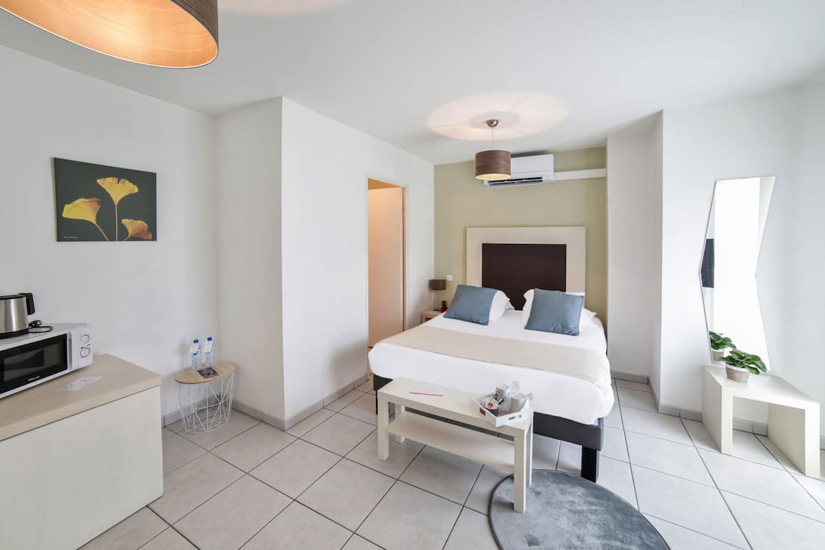 Ein modernes Hotelzimmer mit Bett, Nachttisch, Lampe, Klimaanlage und einem kleinen Schreibtisch mit einer Mikrowelle.